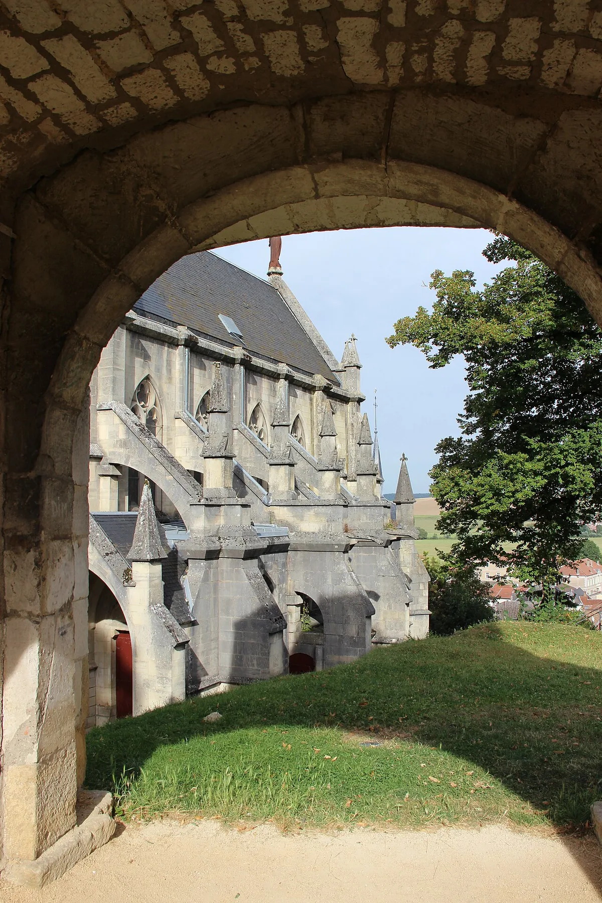 The chapelle castrale at Vaucouleurs framed within the stone arch of the Porte de France, with grass and trees between them.