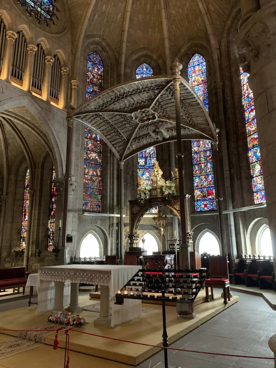 The apse of the collegiate church at Roncesvalles: the silver image of Our Lady beneath a metal canopy above the altar, with tall windows of colored glass behind and candles before the sanctuary.