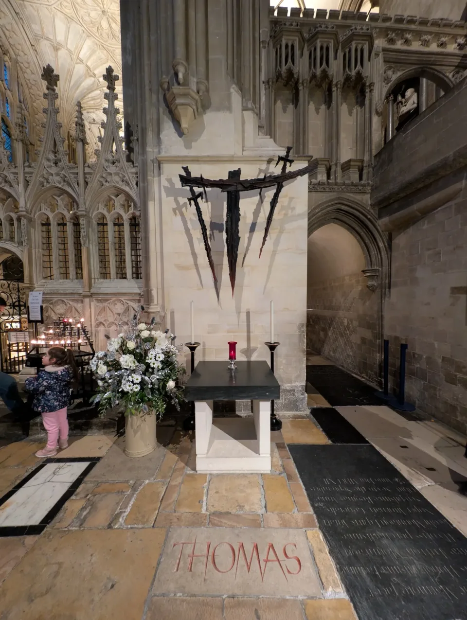 The Martyrdom at Canterbury Cathedral: a plain stone altar beneath a sculpture of jagged swords, with THOMAS cut in red letters in the floor.