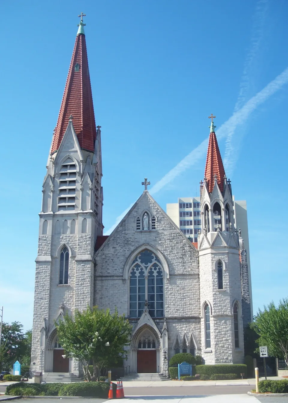 The front facade of the Basilica of the Immaculate Conception, its two unequal stone towers rising to red tiled spires above a pointed-arch window and triple doors.