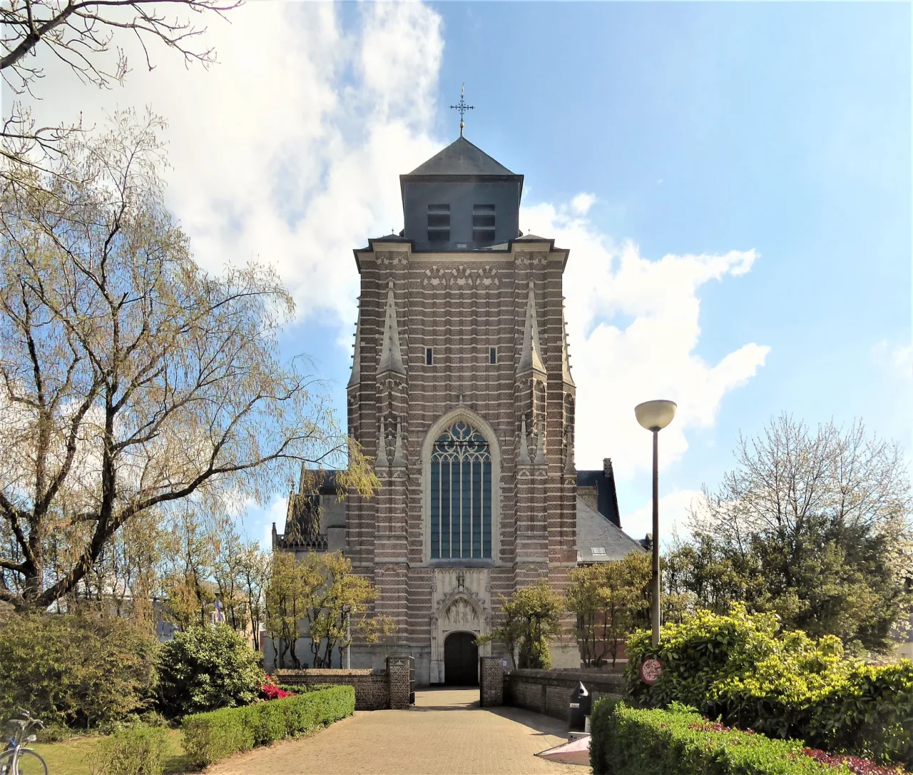 The west front of the Sint-Dimpnakerk at Geel, its massive unfinished tower banded in brown ironstone and white sandstone above an open door.