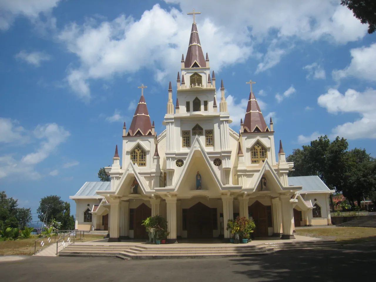 The cream facade and twin towers of Larantuka Cathedral, with the strait and the island of Adonara behind.