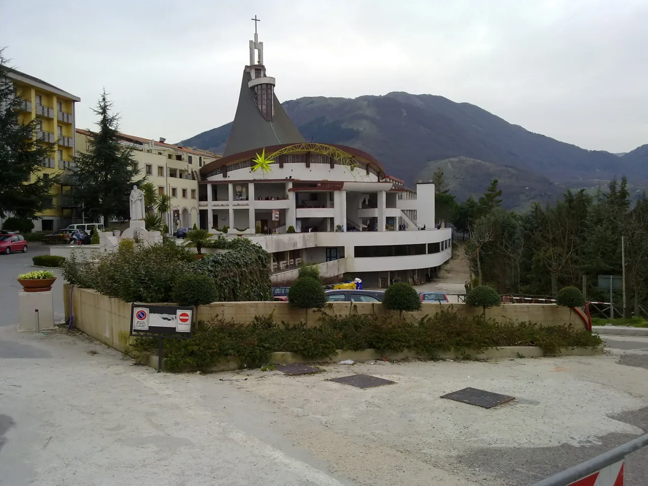 The tent-shaped Church of the Redeemer at Materdomini seen from the road below, its dark conical roof and cross-topped spire against the wooded hills of Alta Irpinia.