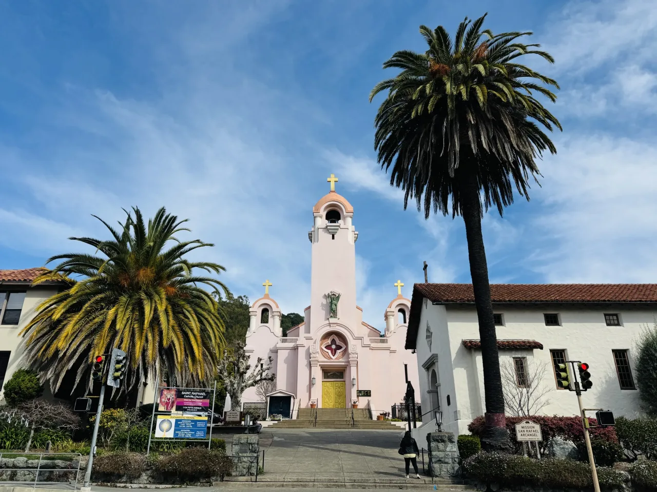 The pink parish church of St. Raphael with the white reconstructed mission chapel beside it, framed by palms in San Rafael.