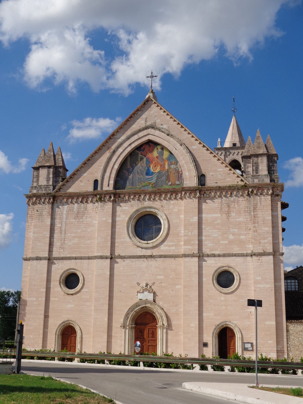 The painted facade and bell gable of the Santuario di Rivotorto in the Assisi valley.