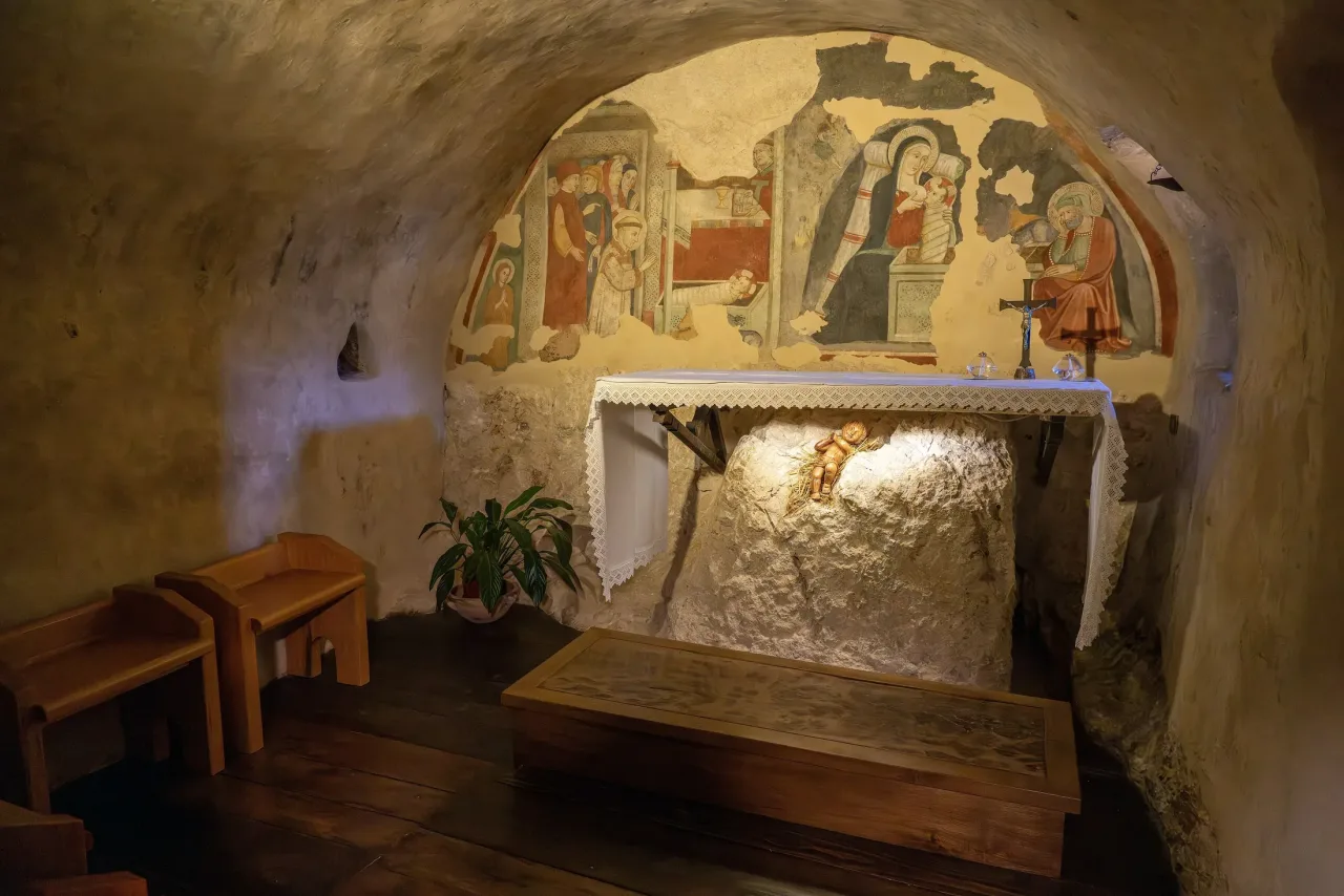 The Chapel of the Crib at Greccio: a rock cave with an altar over the bare rock and a fresco of the Nativity on the curved wall above.