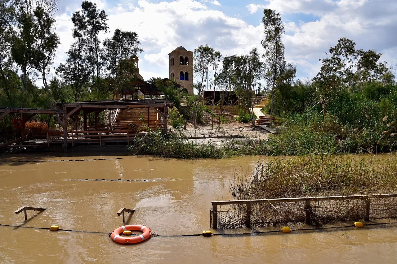 The narrow Jordan River flowing through reeds at Al-Maghtas on the Jordanian bank.