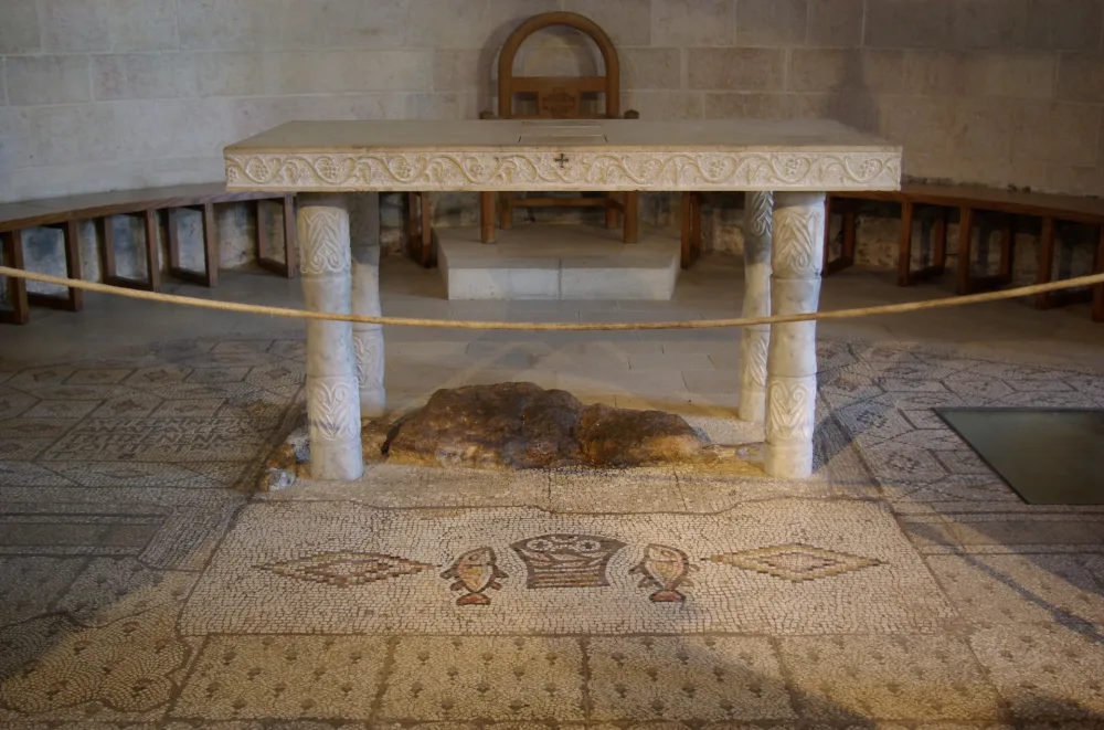 The stone altar at Tabgha over a rough rock, with the small mosaic of a bread basket between two fish set into the floor in front.