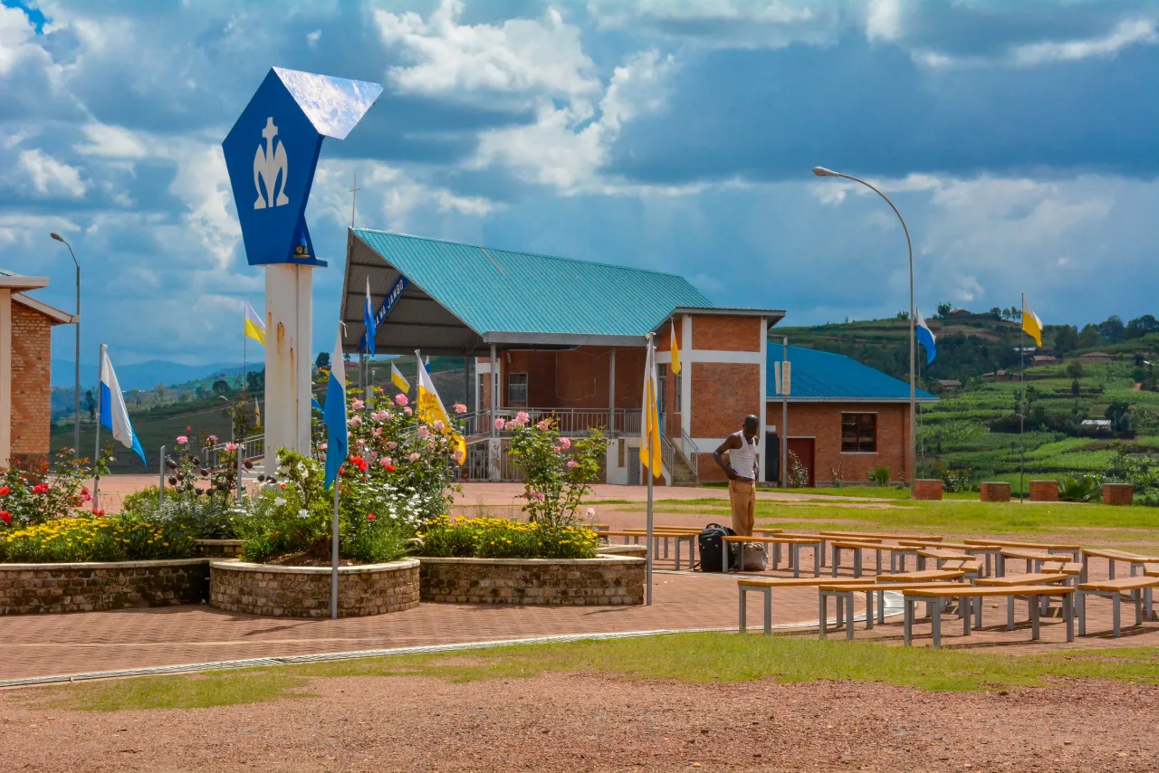 The apparition plaza at Kibeho, with the Nyina wa Jambo sign, benches for pilgrims, and the chapel of Our Lady of Sorrows beyond.