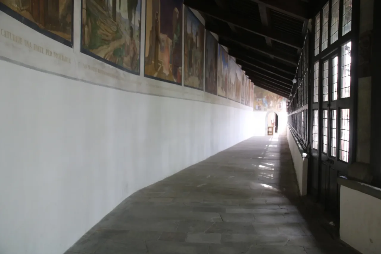 The long covered Corridor of the Stigmata at La Verna, with painted scenes from Francis's life along the wall and windows on the other side.