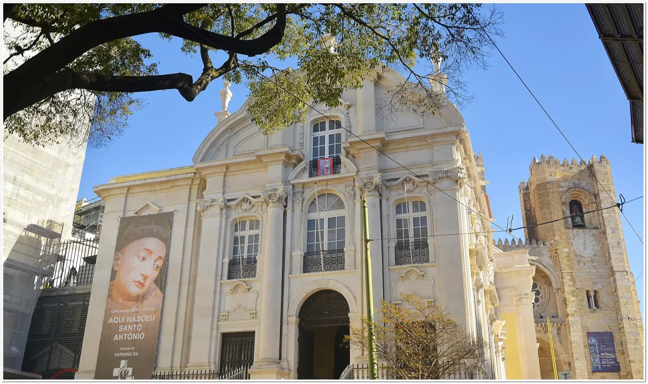 The Baroque facade of the Church of Saint Anthony in Lisbon, with the crenellated tower of the cathedral rising just beyond it.