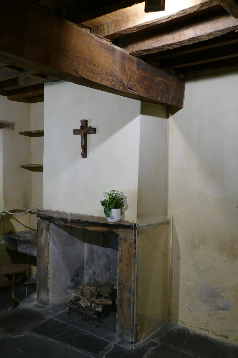 The small interior of the Cachot in Lourdes, with low beams, a hearth, and a crucifix.