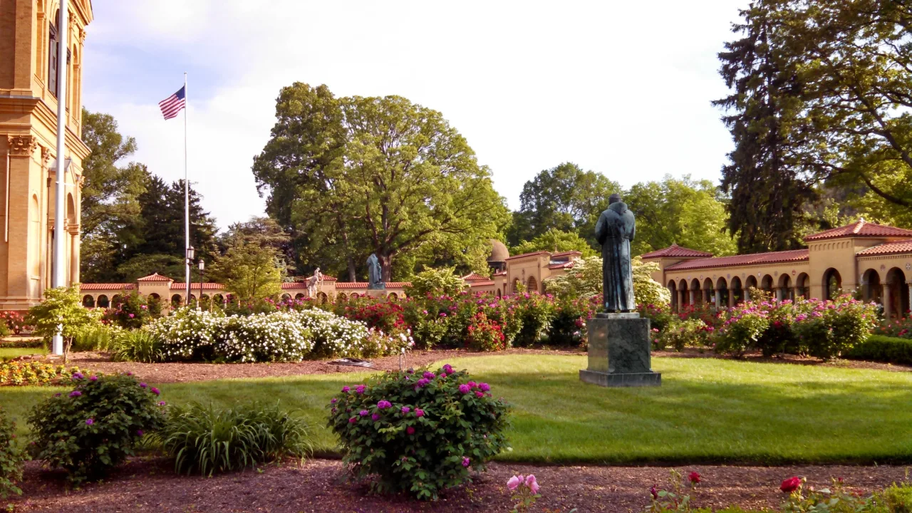A Marian statue and circular stone pool within the green gardens of the Franciscan Monastery in Washington.