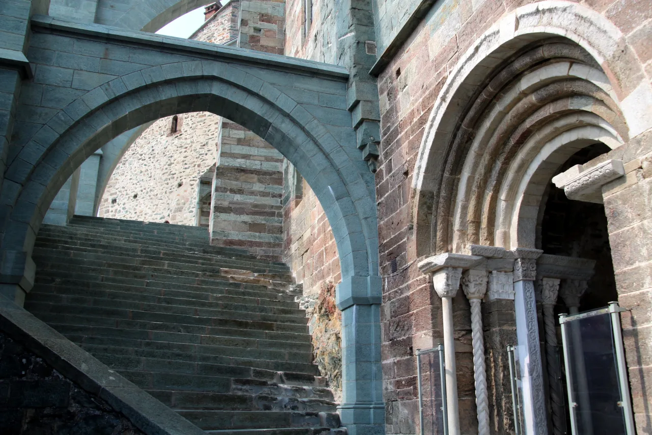 The arched entrance to the Sacra church beside an outdoor staircase and beneath flying buttresses.