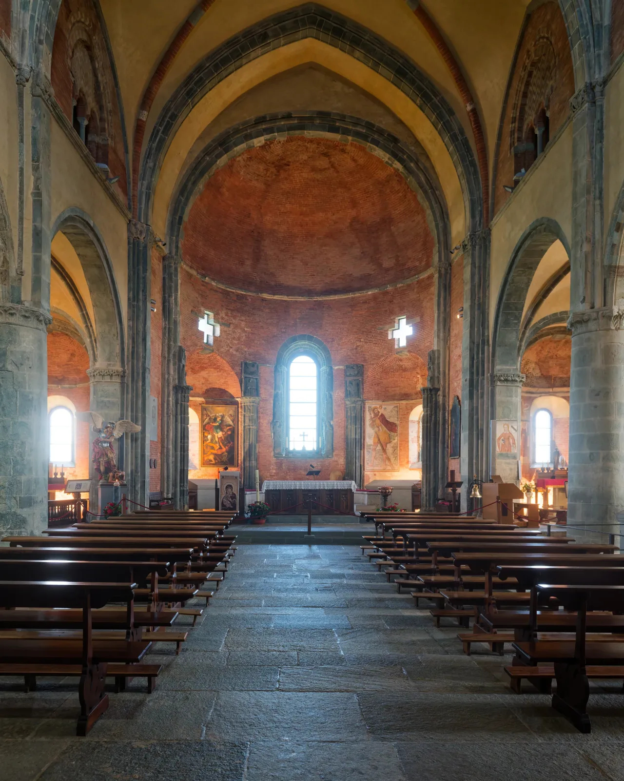 The nave and sanctuary of the Sacra church, with high stone arches, pews and the altar ahead.