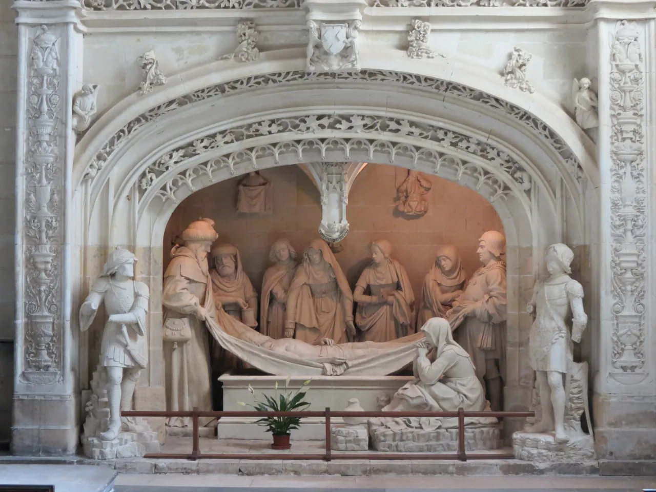 Christ’s body in the carved Entombment at Solesmes, surrounded by mourners beneath an ornate stone arch.