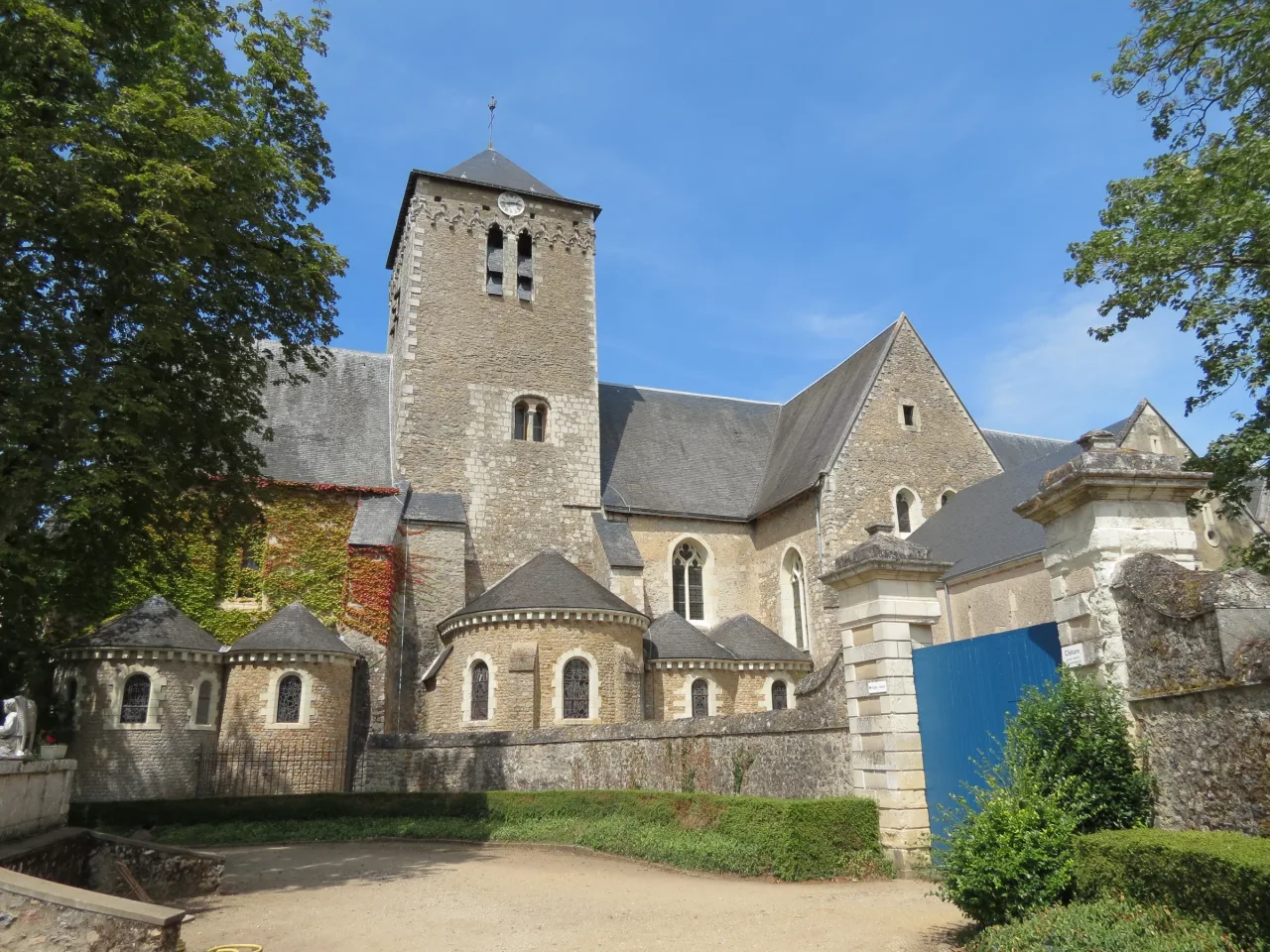 Stone church tower, roof and chapels of Saint-Pierre de Solesmes seen from outside the abbey wall.