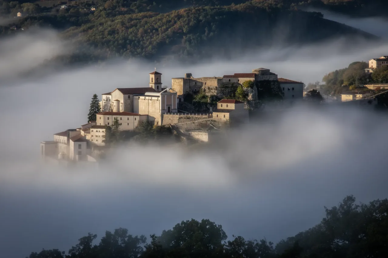 The historic center of Muro Lucano at dawn, its bell tower and hillside houses rising out of a bank of mist below the medieval castle.