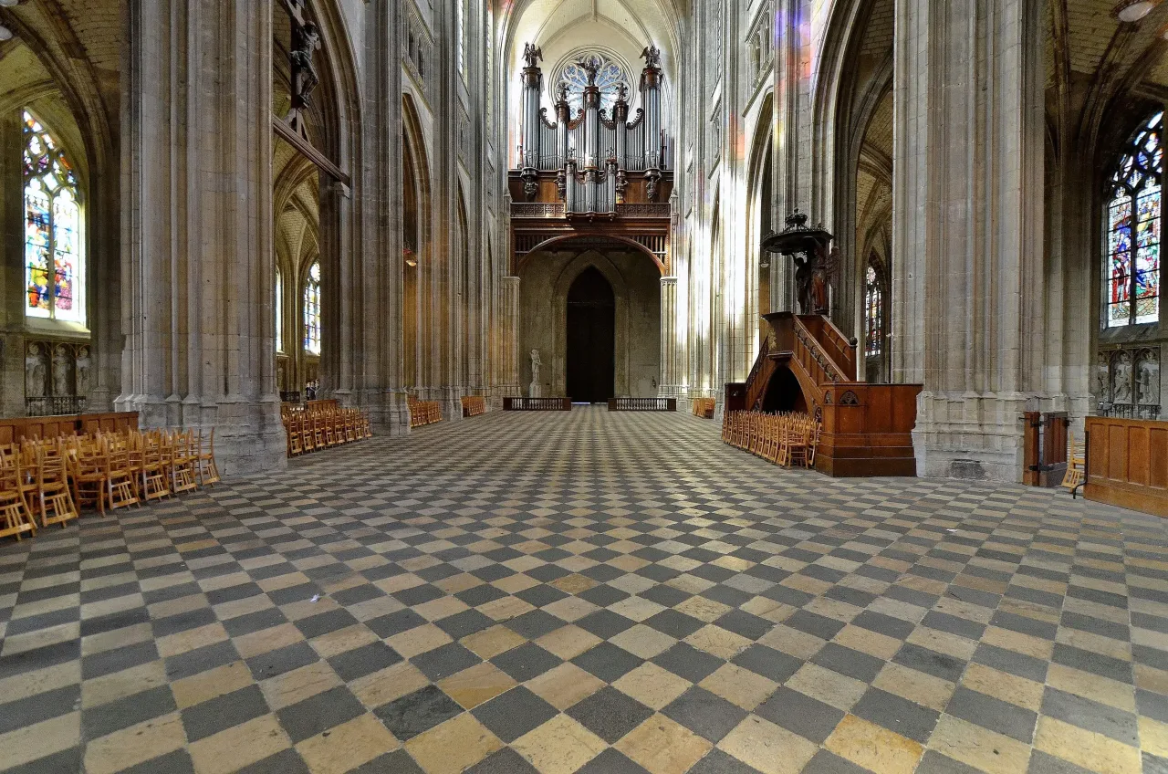 The nave of Sainte-Croix in Orleans looking west toward the organ, with a chequered stone floor, tall arcades and stained glass in the aisles.