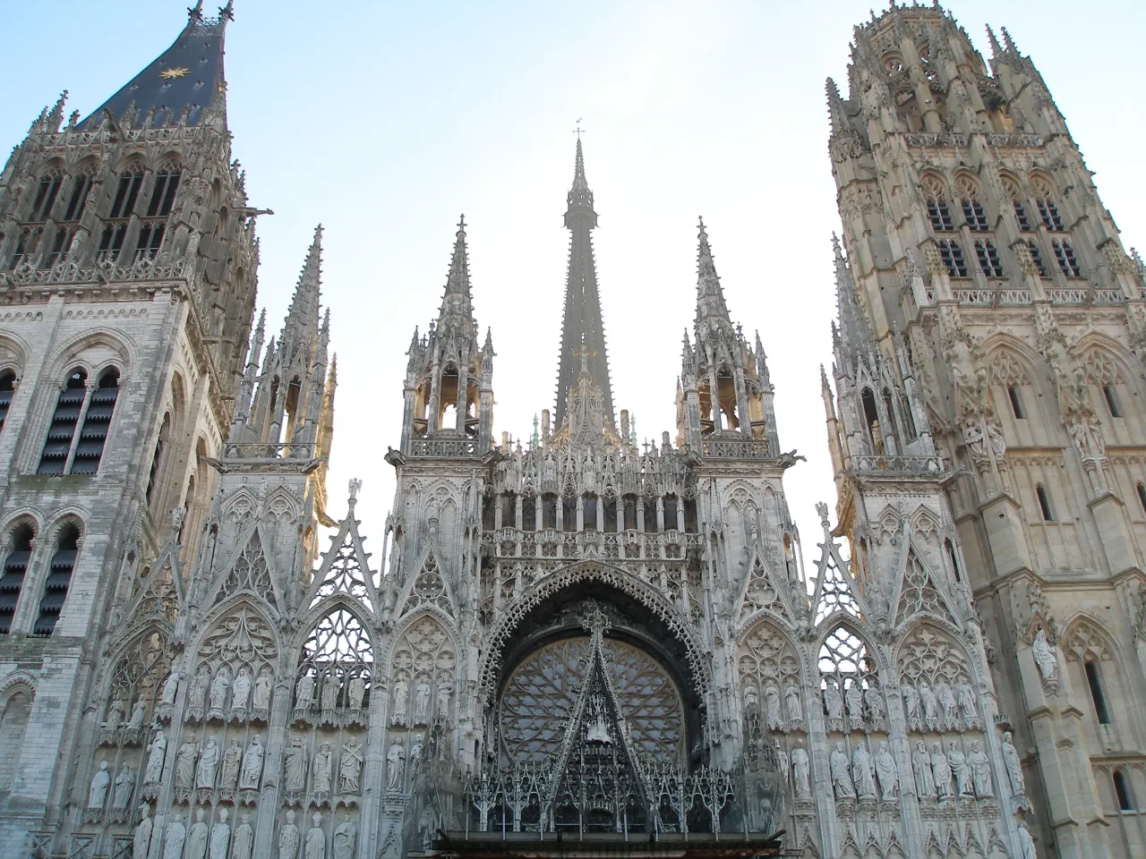 The upper stage of the west front of Rouen Cathedral in morning light, its gable and openwork spirelets rising between the two unmatched western towers.