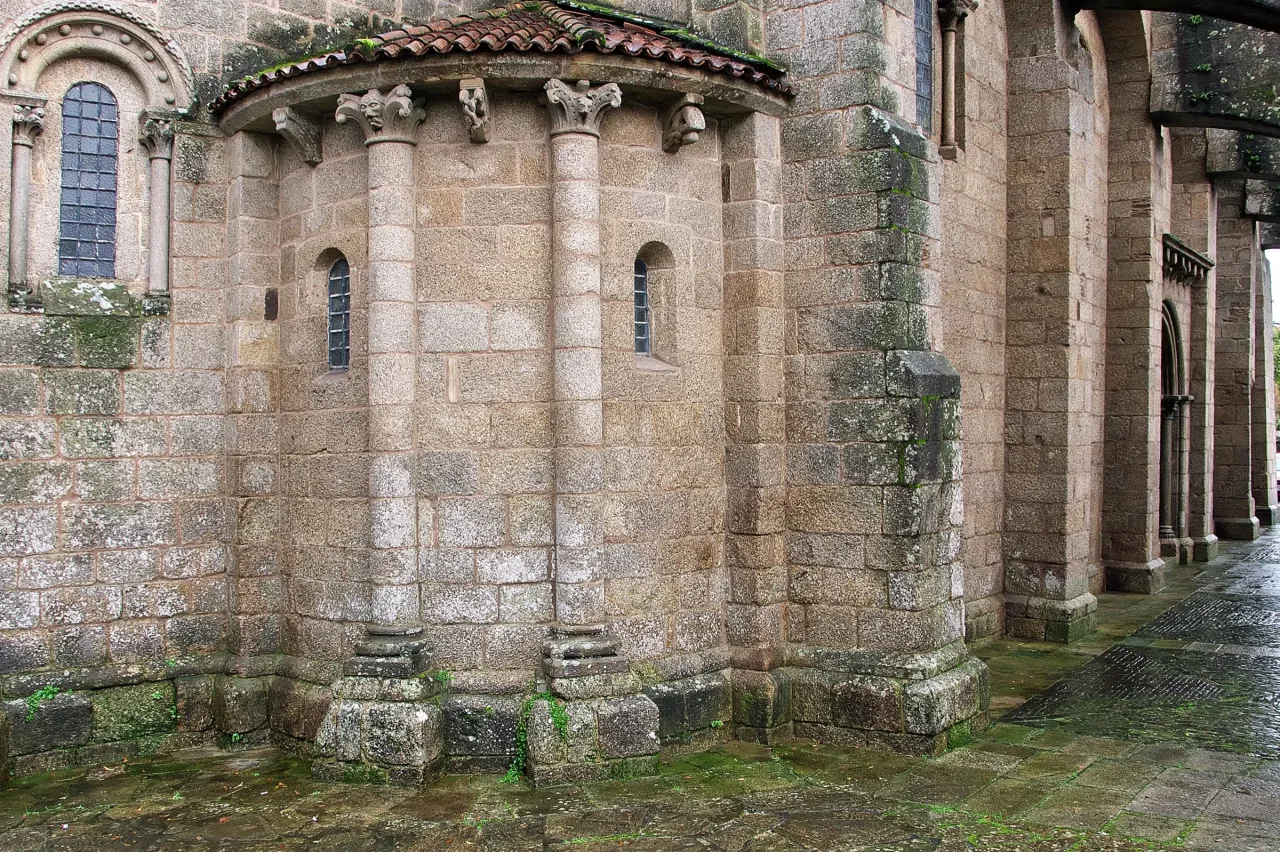 The granite apse and northern flank of the collegiate church of Santa María a Real do Sar, with carved corbels under the eaves and heavy buttressing alongside.