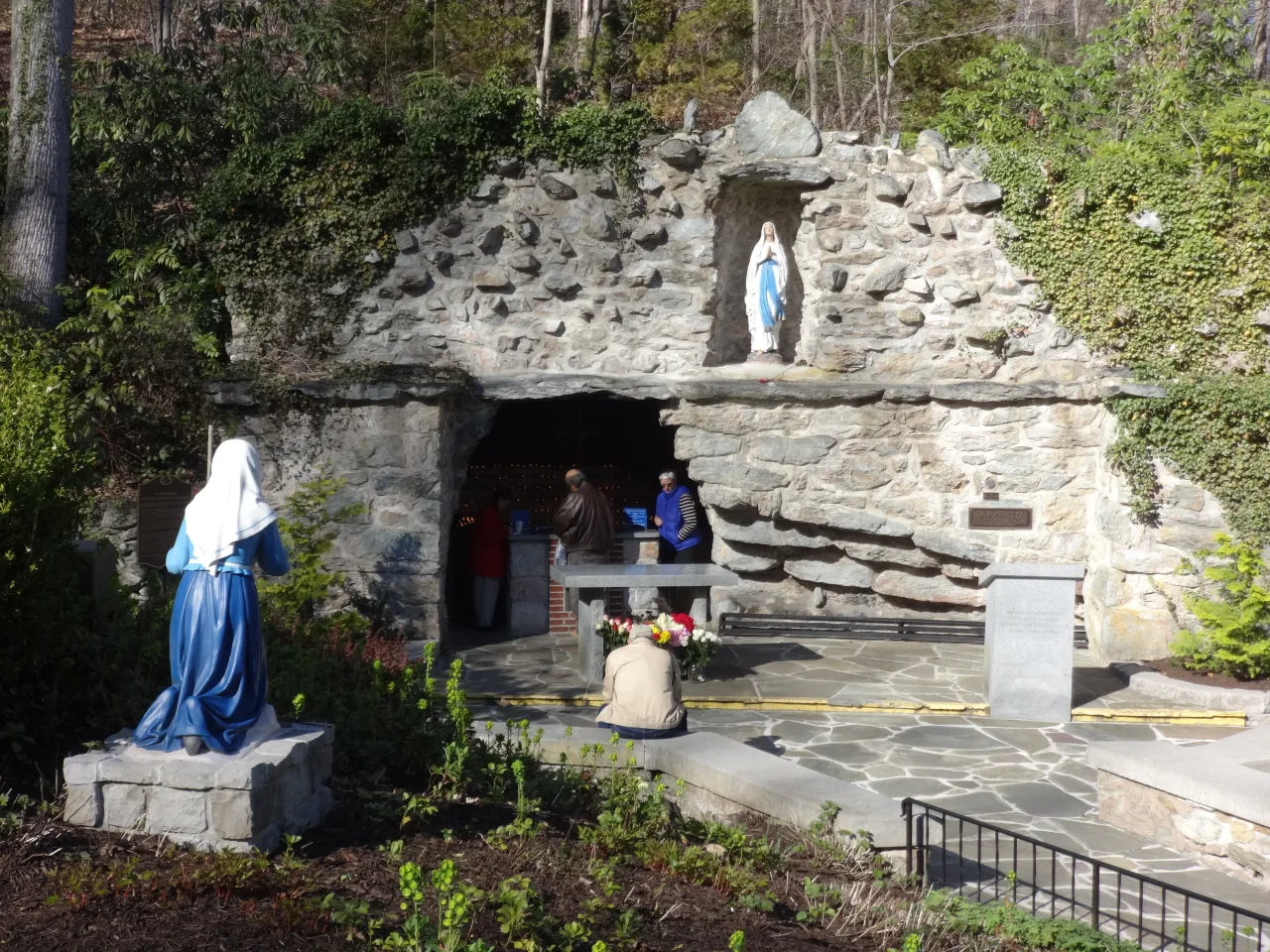 The stone Lourdes grotto in Emmitsburg with statues of Our Lady and Saint Bernadette above an outdoor altar and rows of benches.