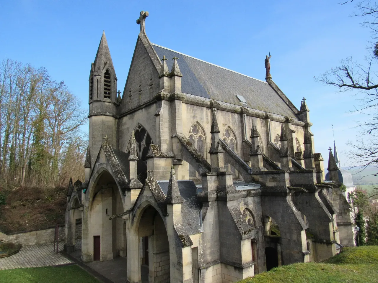 The chapelle castrale at Vaucouleurs seen along its flank, a stone chapel with buttresses, pinnacles and a steep slate roof above a grass slope.