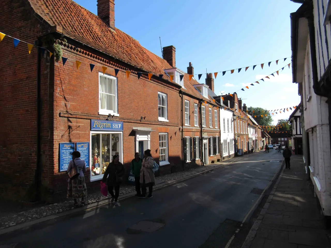 High Street in Little Walsingham, with brick buildings, pilgrims and bunting.